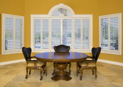 A dining room with beautiful white blinds on the yellow shade walls